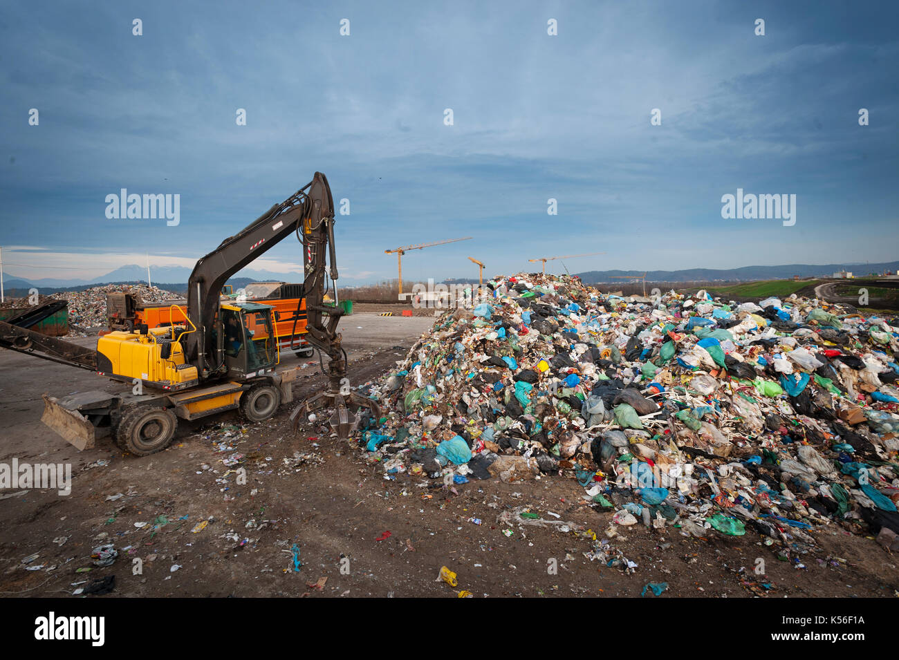 Bulldozer con brazo mecánico agarrando por un montón de residuos en el relleno sanitario de la ciudad. La gestión de los residuos, ecología concepto. Foto de stock