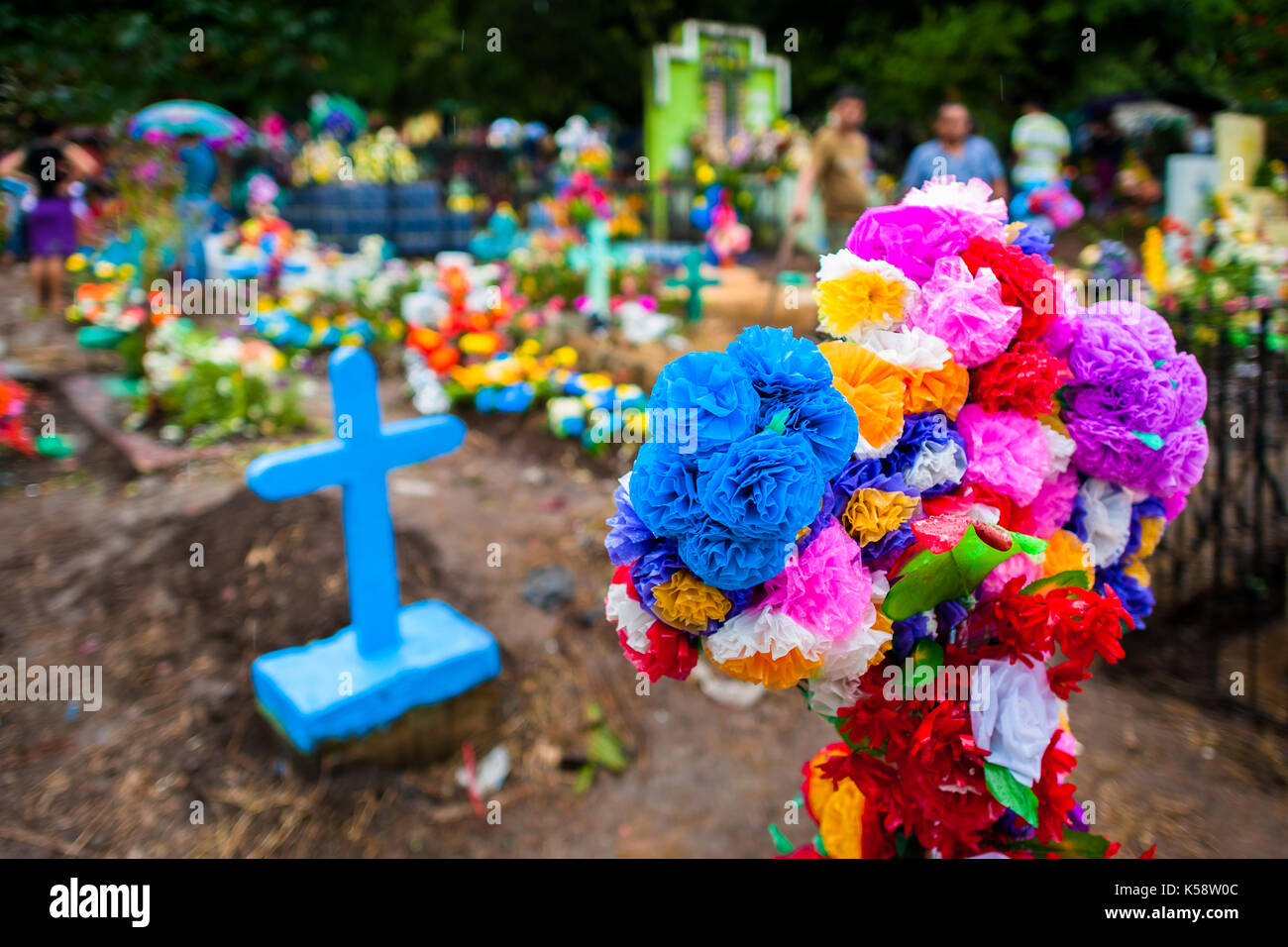 Una cruz, tumbas decoradas con coloridas flores de papel, se observa durante la celebración del