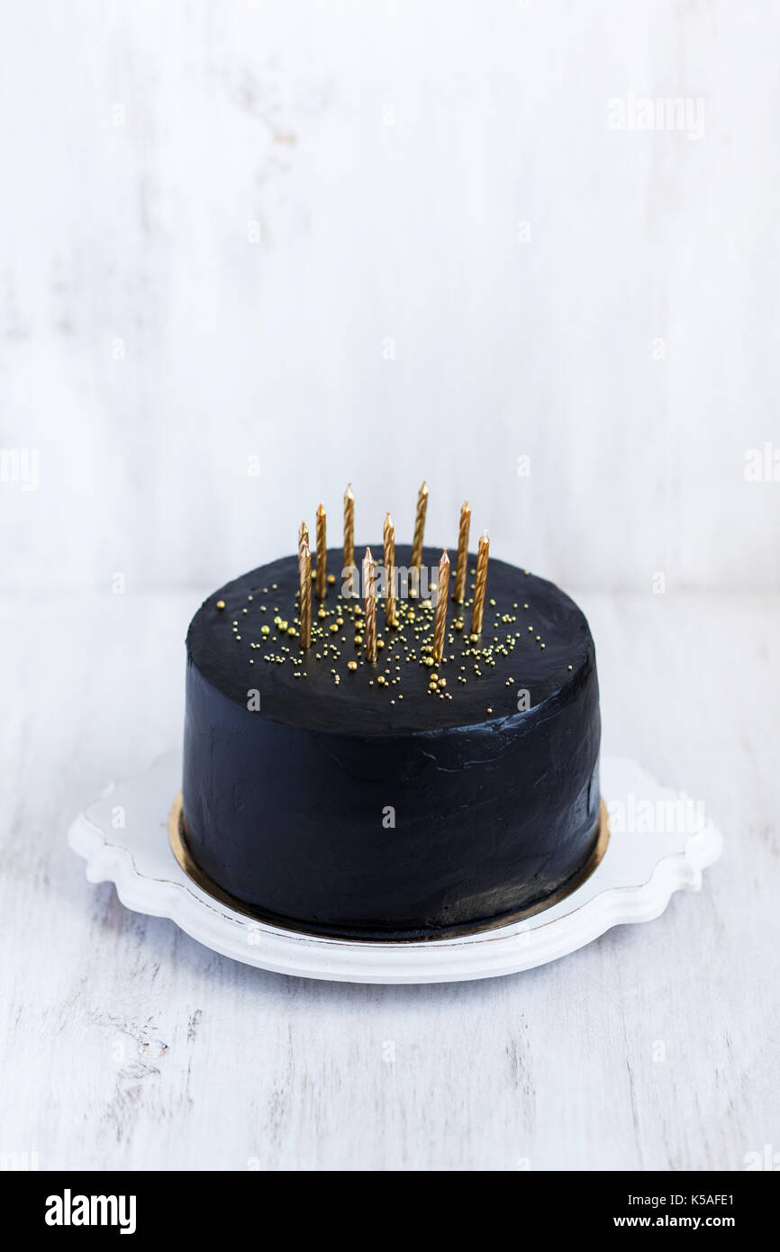Negro tarta de cumpleaños con velas de oro sobre fondo blanco. Foto de stock