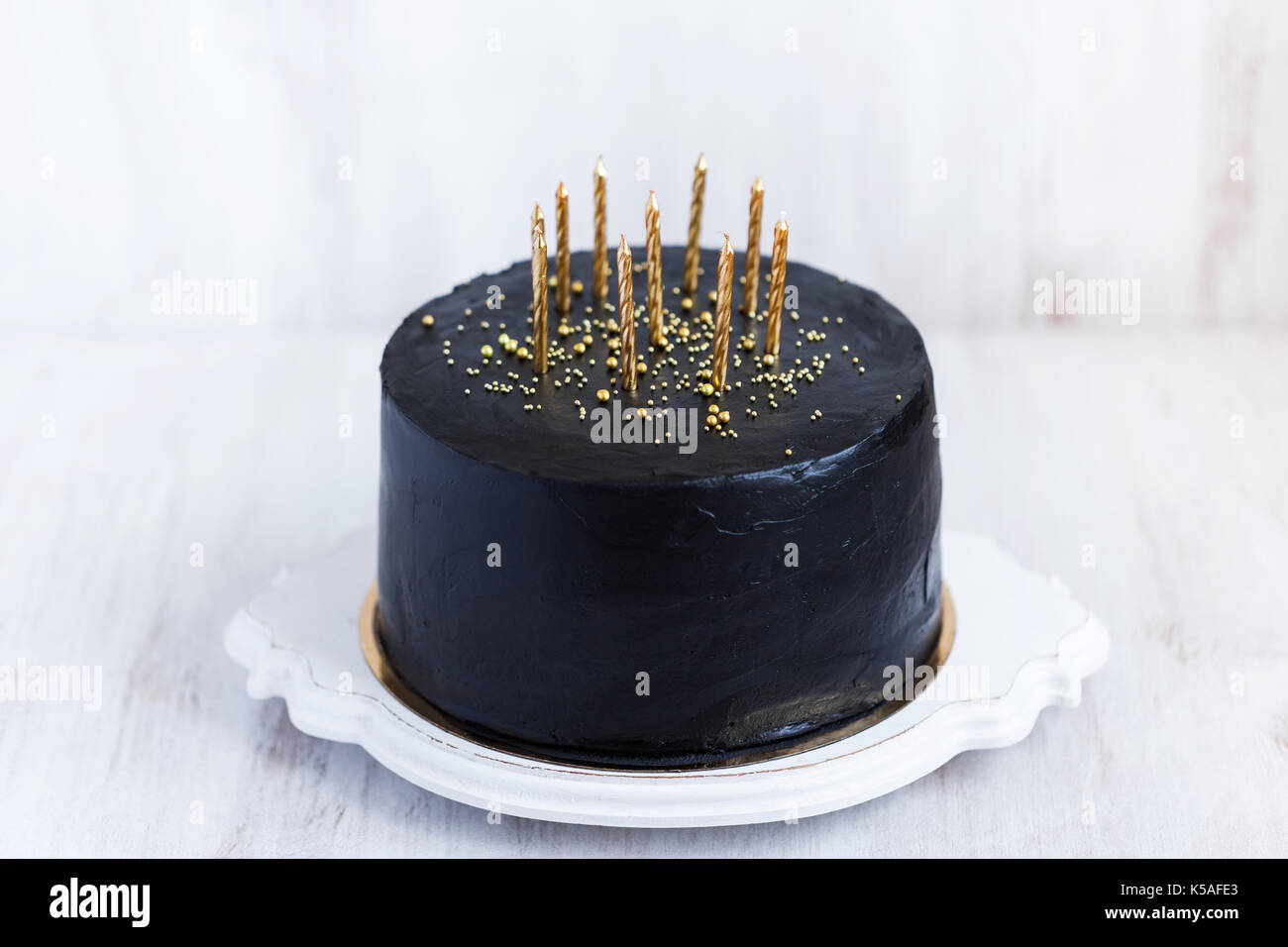 Negro tarta de cumpleaños con velas de oro sobre fondo blanco. Foto de stock
