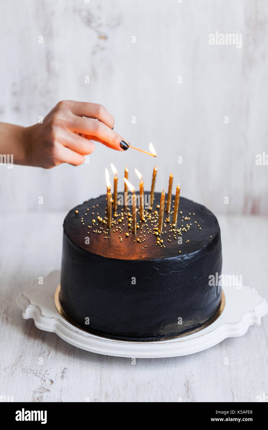 Negro mujer tarta de cumpleaños con velas encendidas, mano de fondo blanco. Foto de stock