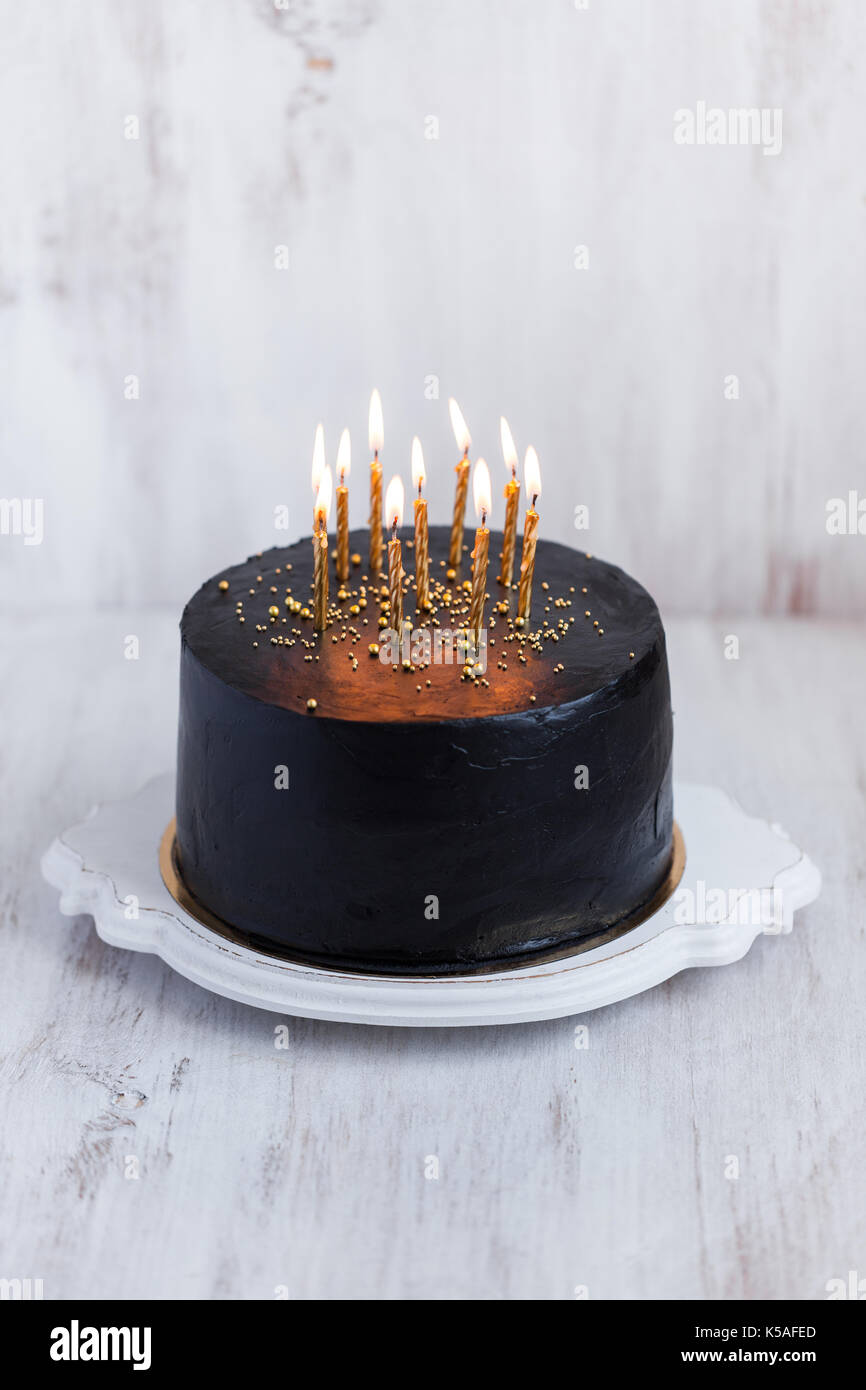 Redondo negro tarta de cumpleaños con la quema de velas de oro sobre fondo blanco. Foto de stock