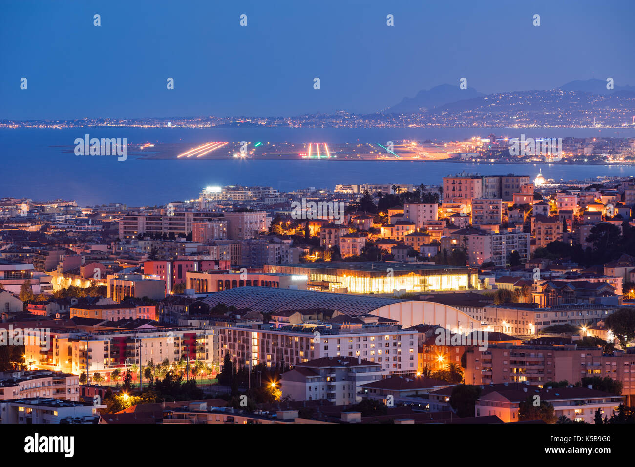 Vista elevada de tejados de Niza en penumbra con las pistas de aterrizaje en la distancia. Riviera francesa, Provence-Alpes-Côte d'Azur, Francia Foto de stock