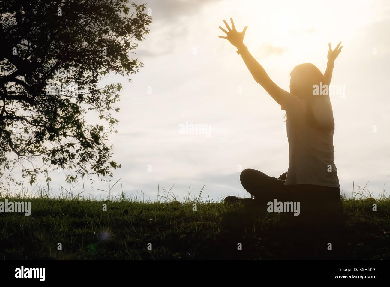 Una feliz mujer asiática es relajante sobre hierba verde y levantó los brazos hacia el cielo en un día soleado de verano con parque de fondo. concepto de bienestar y salud l Foto de stock