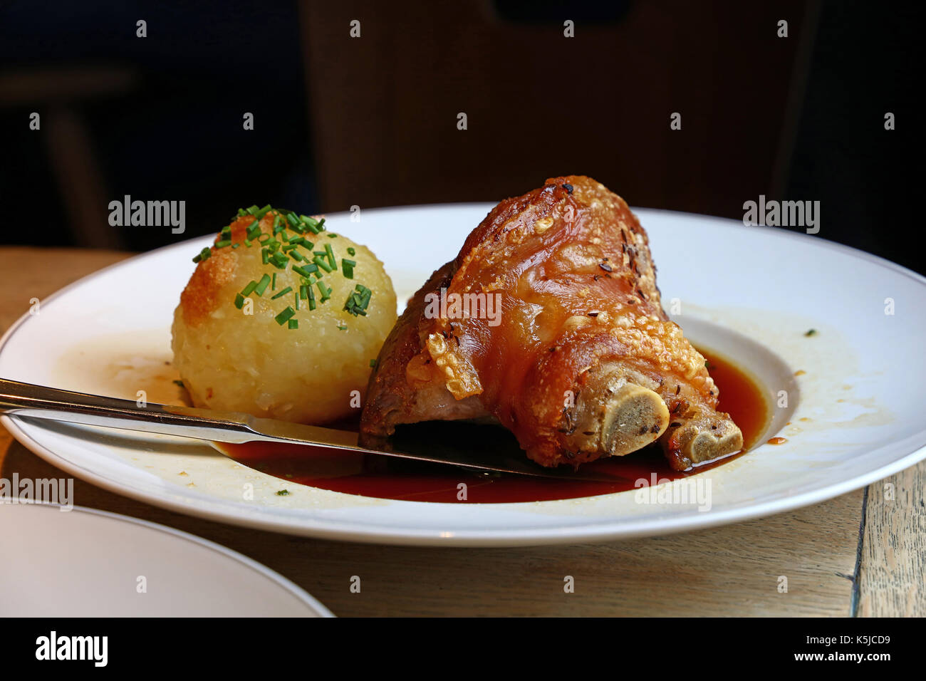 Porción de asado de cerdo suculento avance pivote o mango con cebollino y dumplings de Baviera en la placa sobre la mesa, cerrar, bajo ángulo de visión Foto de stock