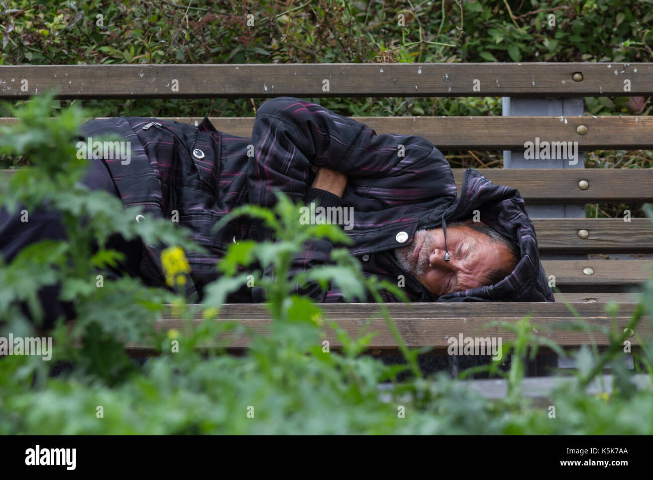 Kazan, Rusia - 9 septiembre 2017: homeless alcohólico hombre es mendigo durmiendo en un banco en el parque Foto de stock