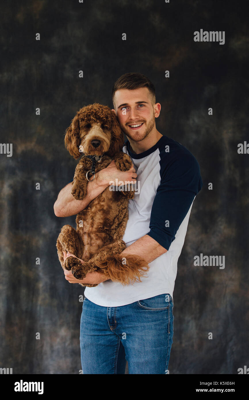 El hombre con su perro mascota en sus brazos. Ellos están de pie frente a  un estudio de fondo y están mirando a la cámara Fotografía de stock - Alamy