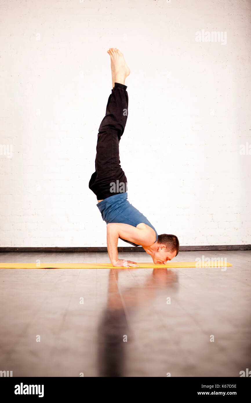 Un joven hombre fuerte haciendo ejercicios de yoga - salamba sirsasana padmasana, pino con piernas. Foto de stock