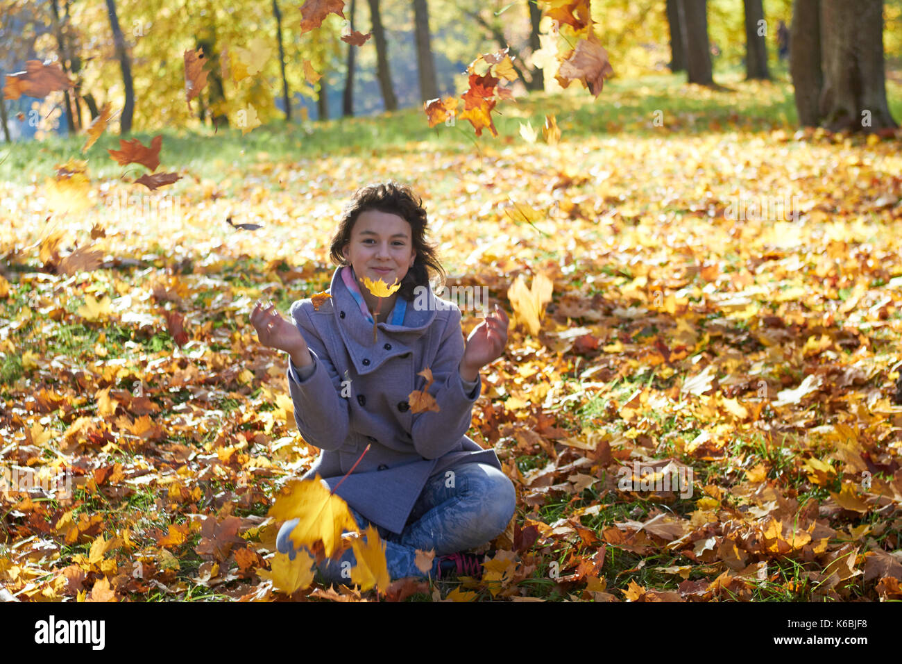 Feliz adolescente chica en el paisaje del otoño lanzando hojas Foto de stock