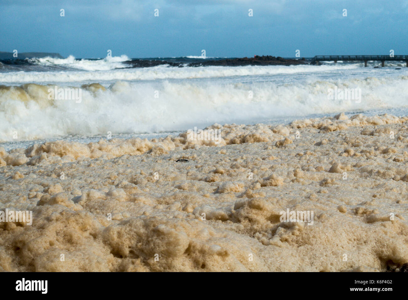 Cielos nublados, wild seascape y espuma de mar o spume lavando los Pebble Beach en carrickmore rd, ballycastle, BT54, Irlanda del Norte, reino unido Foto de stock