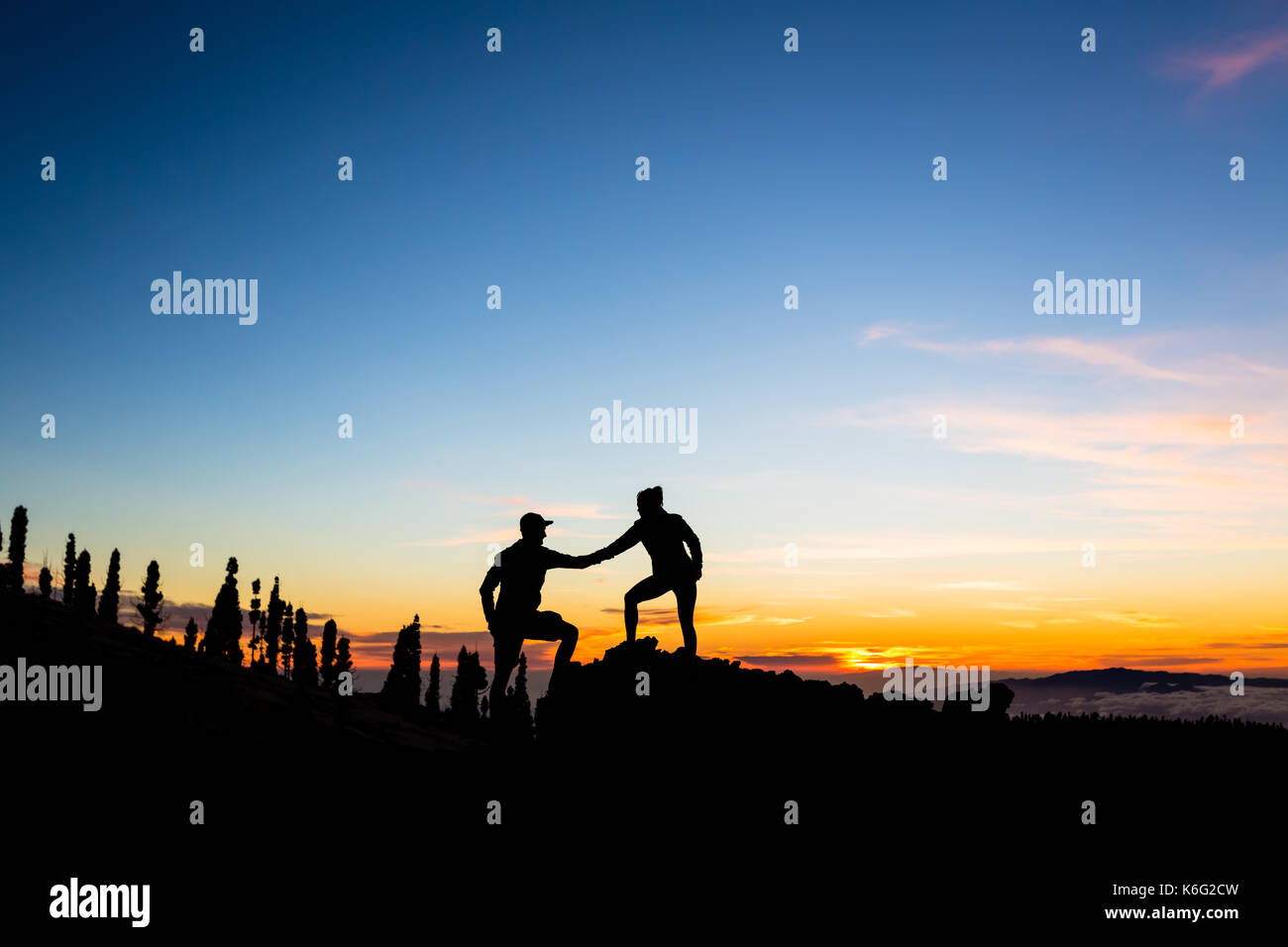 Trabajo en equipo pareja con mano de ayuda y confianza. Silueta de equipo ayuda a través de las montañas del atardecer. Un hombre y una mujer excursionistas o montañeros alcanzar metas en Trabajo en equipo pareja con mano de ayuda y confianza. Silueta de equipo ayuda a través de las montañas del atardecer. Un hombre y una mujer excursionistas o montañeros alcanzar metas en