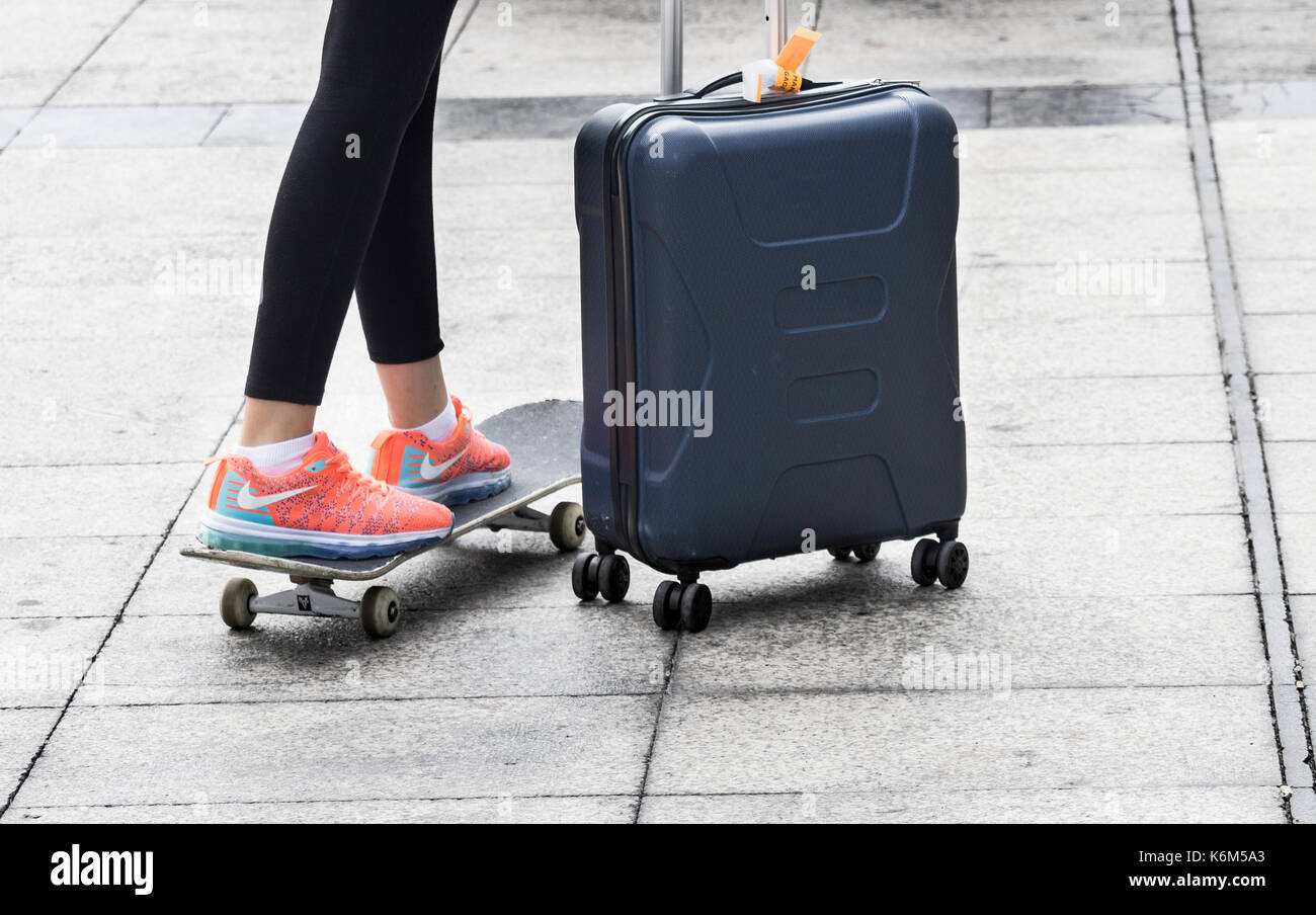 Mujer joven que llevaba zapatillas Nike formadores con maleta con ruedas y  andar en monopatín Fotografía de stock - Alamy