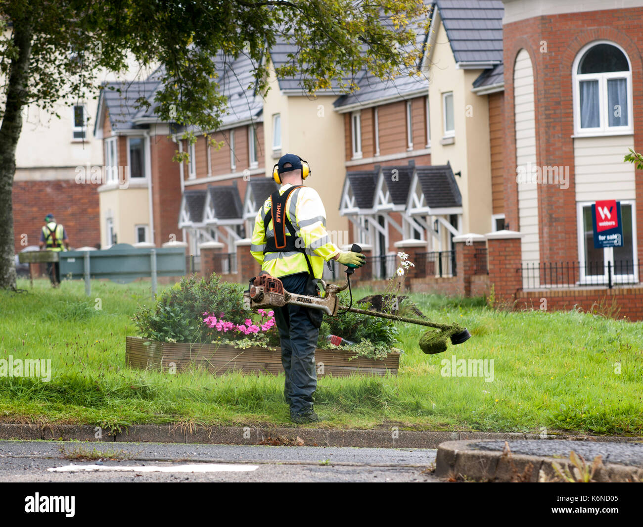 Trabajador en alta vis chaqueta cortando hierba con un gasolina strimmer Foto de stock