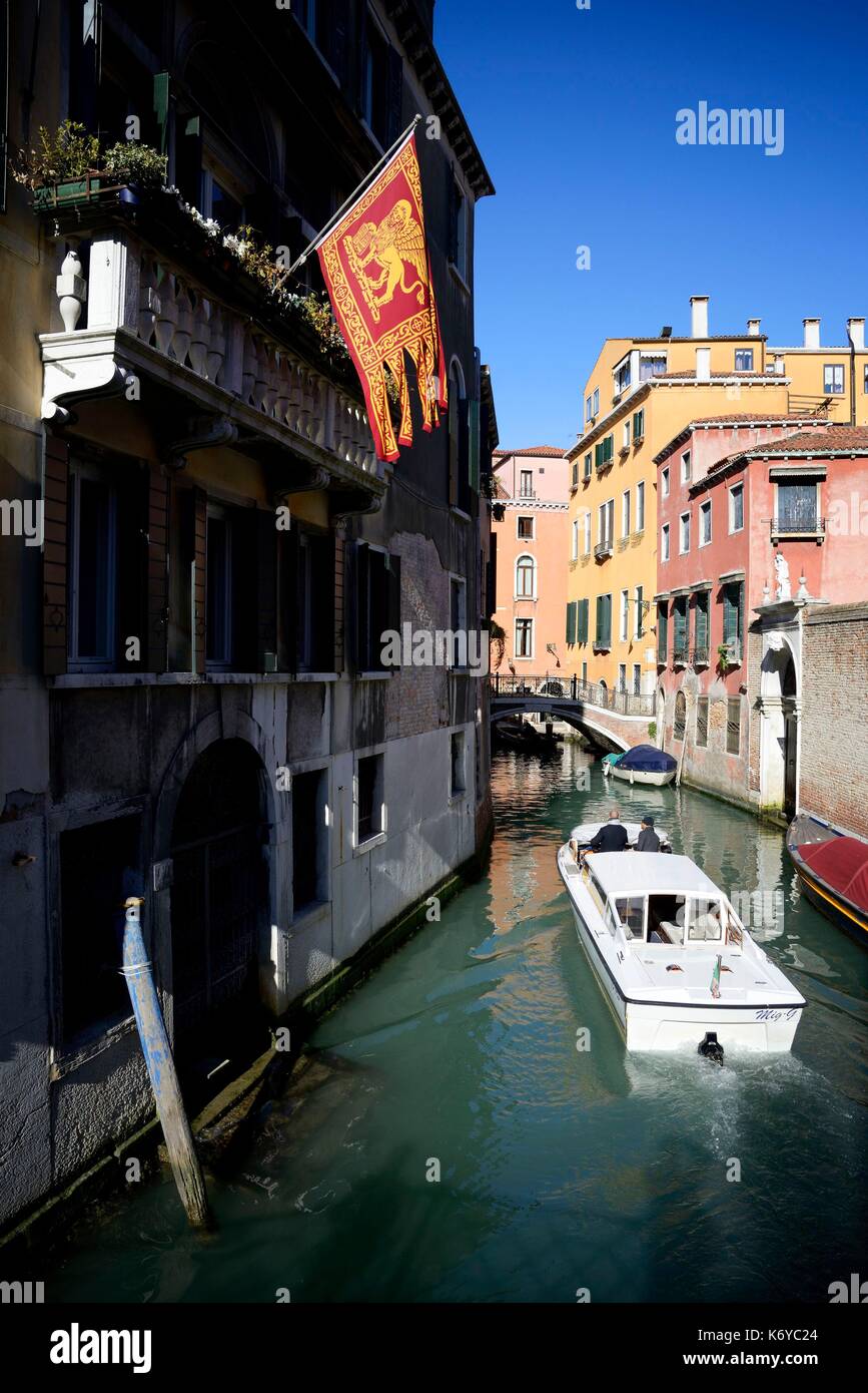 Italia, Veneto, Venecia, catalogada como Patrimonio de la Humanidad por la UNESCO, el barco en un canal veneciano y bandera Foto de stock