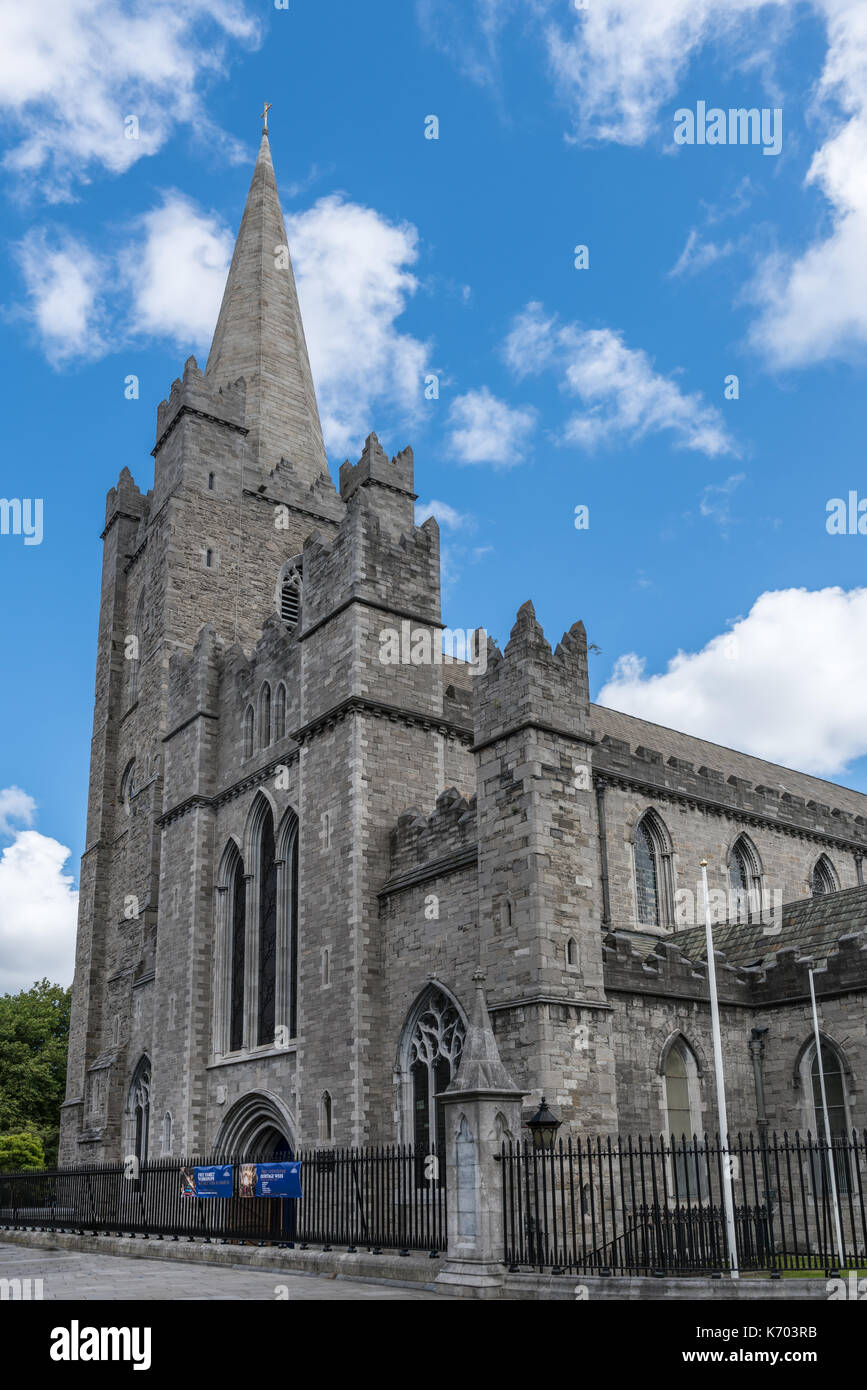 Dublín, Irlanda - Agosto 7, 2017: el campanario de piedra gris y la entrada principal a la catedral de Saint Patrick contra el cielo azul con nubes blancas vegetat verde. Foto de stock