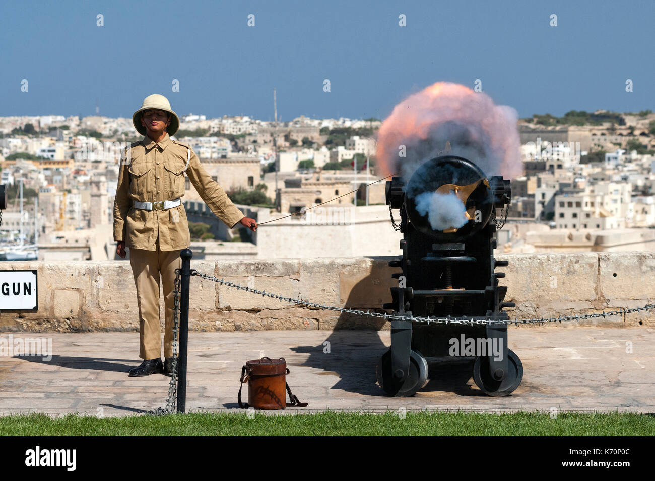 Un joven artillero dispara el cañón de mediodía de Malta para marcar la hora del mediodía. El mediodía cañonazos es una vieja tradición naval que fue restablecido en 2004 y OC Foto de stock