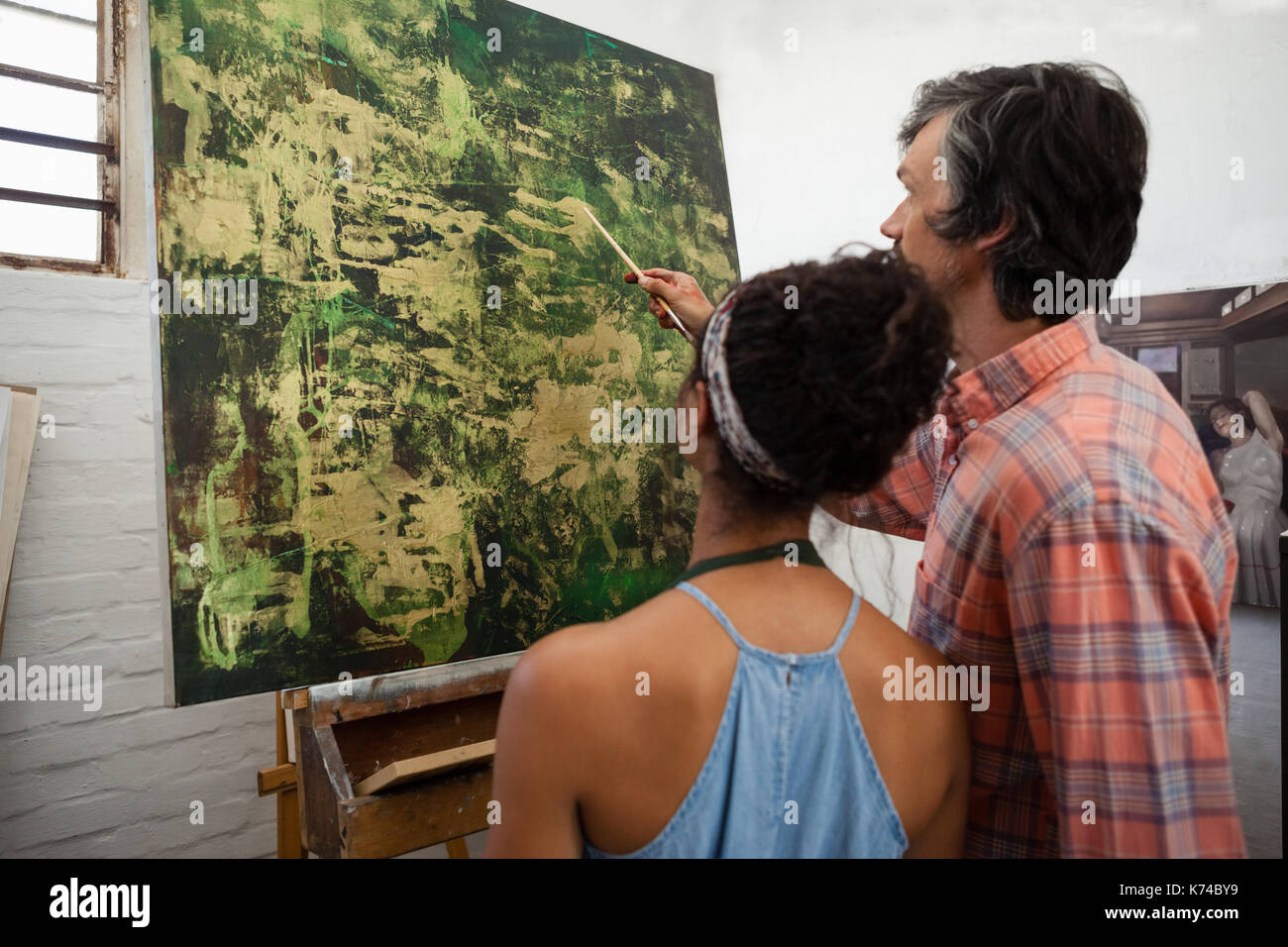 El hombre ayuda a la mujer en la pintura durante la clase de dibujo Foto de stock