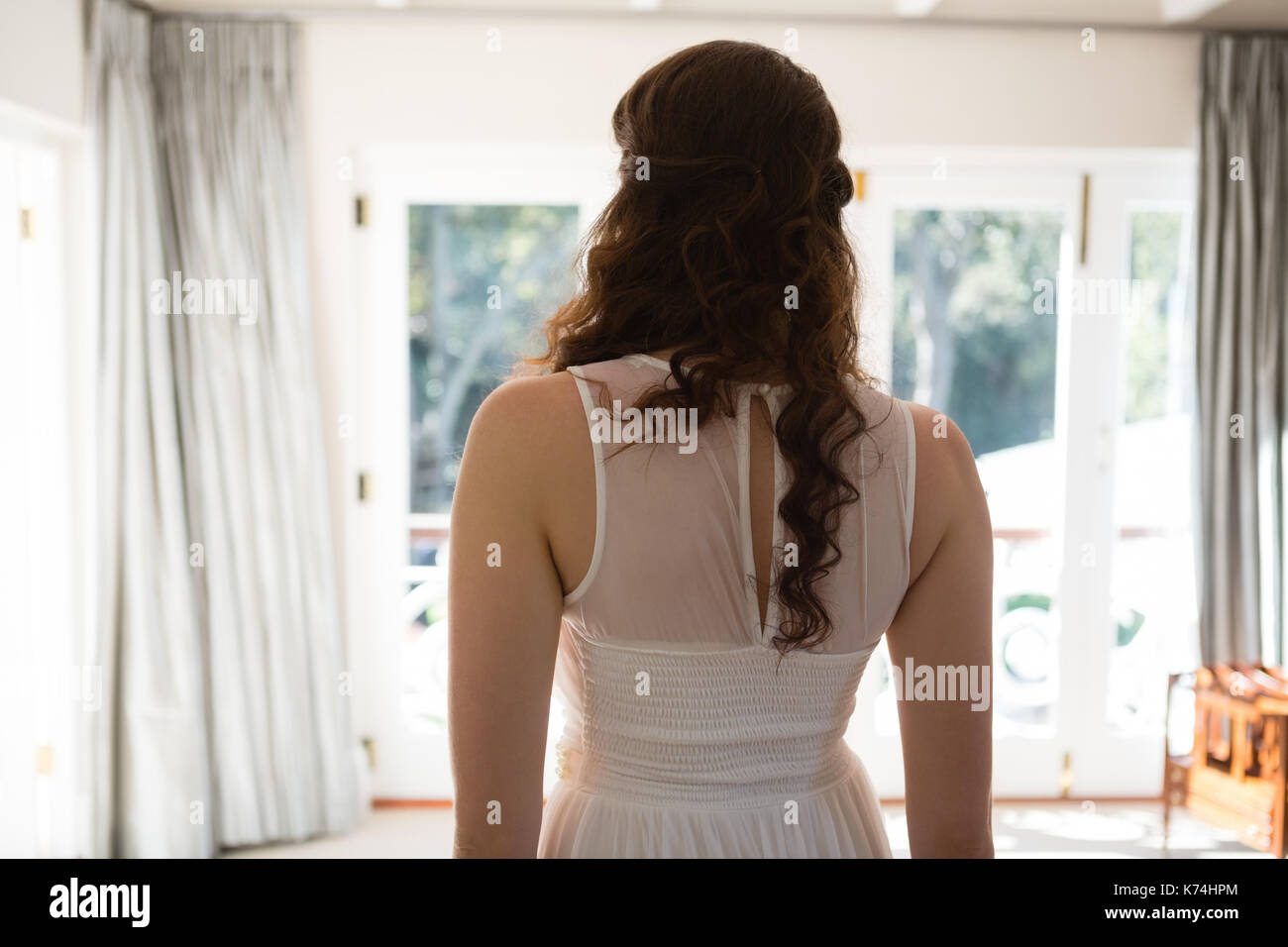 Vista trasera de la novia en traje de novia de pie en casa Foto de stock