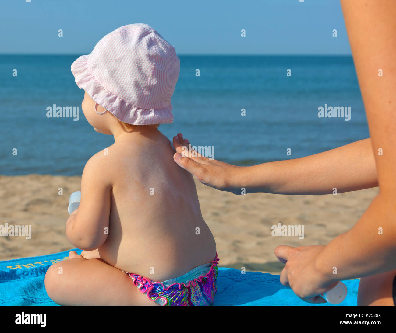 Mom sunscreen pone sobre los hombros de su hija de un año. Foto de stock