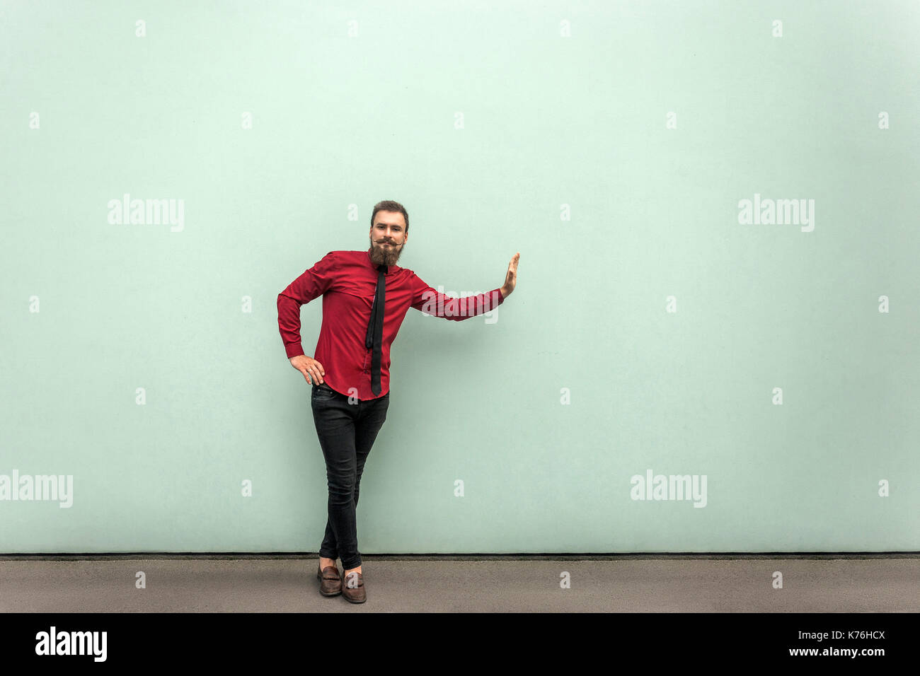Persona de negocios en camisa roja, corbata y pantalones casuales, de pie en la pared gris prop algo invisible al aire libre Fotografía de - Alamy