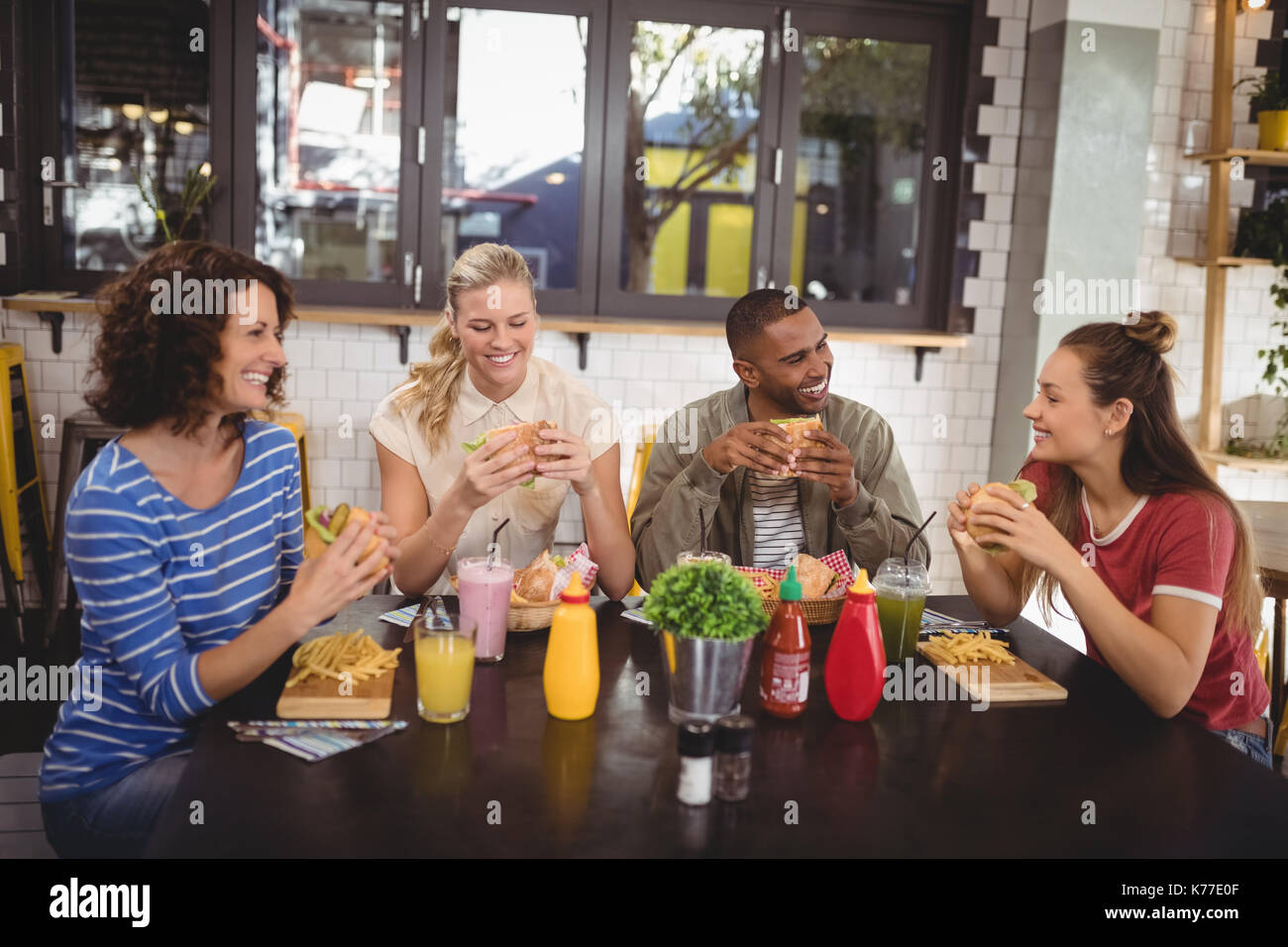 Sonriente joven amigos comer sentado a la mesa en la cafetería Fotografía  de stock - Alamy