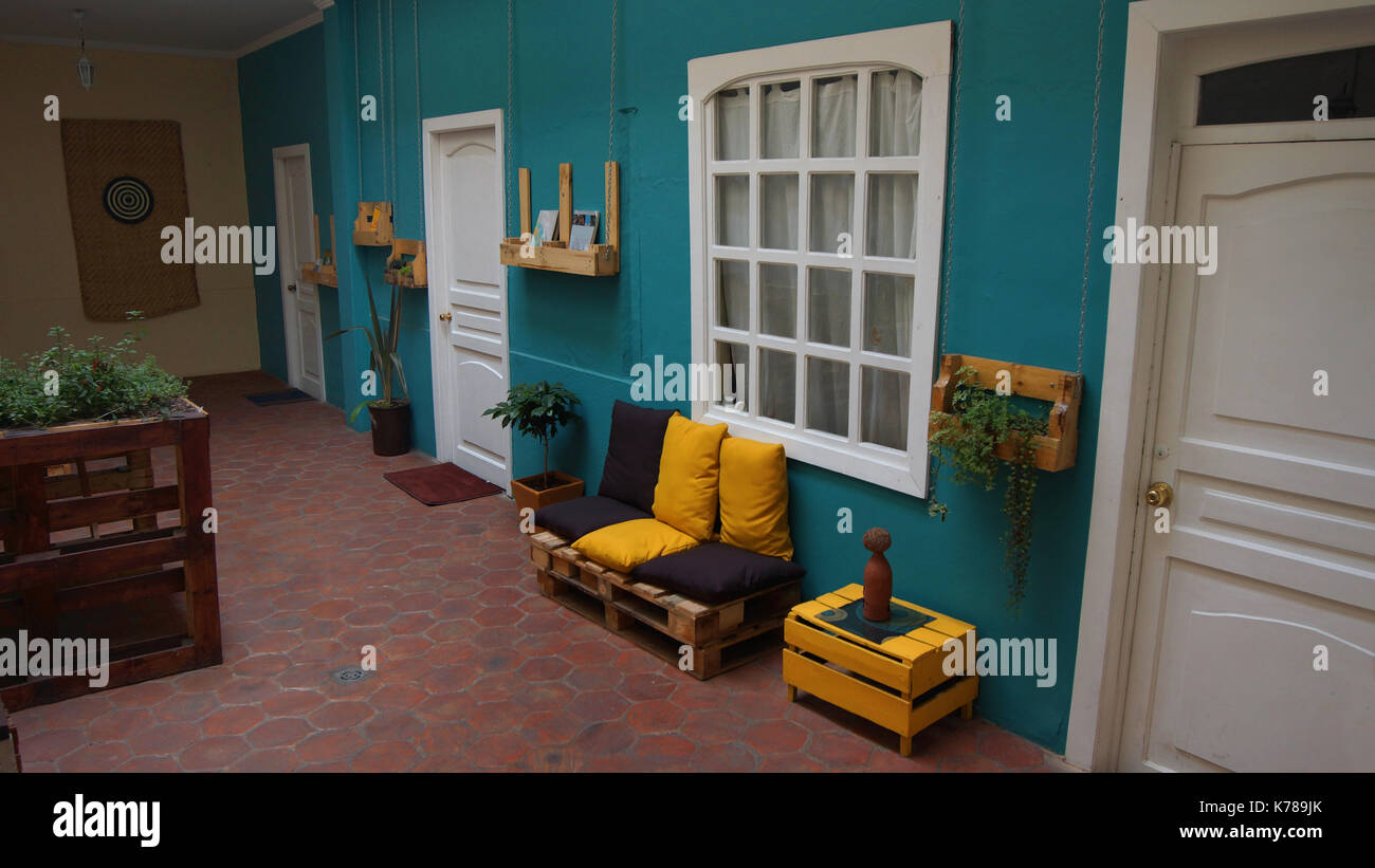 Sofá hecho con tablas rústicas de madera, con cojines amarillos y marrones en una pared verde dentro de una casa Foto de stock