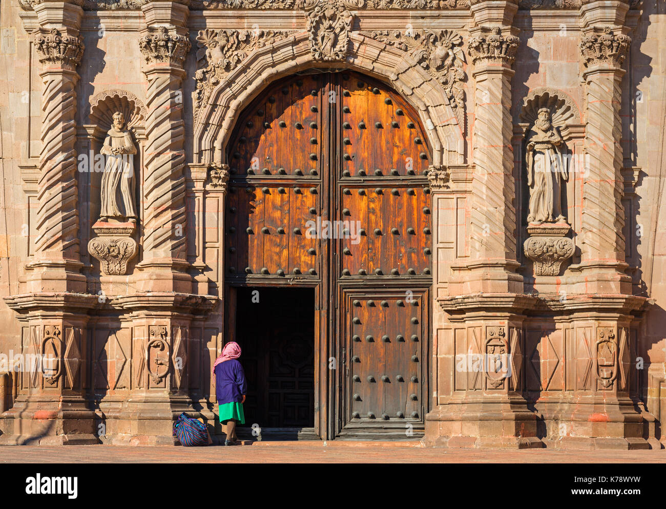 Una mujer indígena a la entrada de una iglesia barroca en el centro de la ciudad de Querétaro, México. Foto de stock