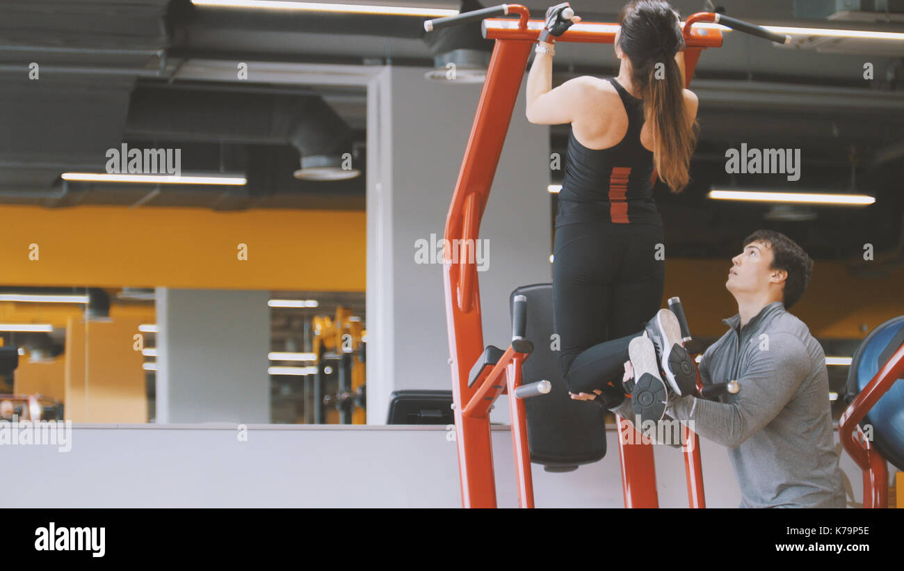Club de fitness - joven realiza pull-ups con entrenador masculino - Vista trasera, cerrar Foto de stock