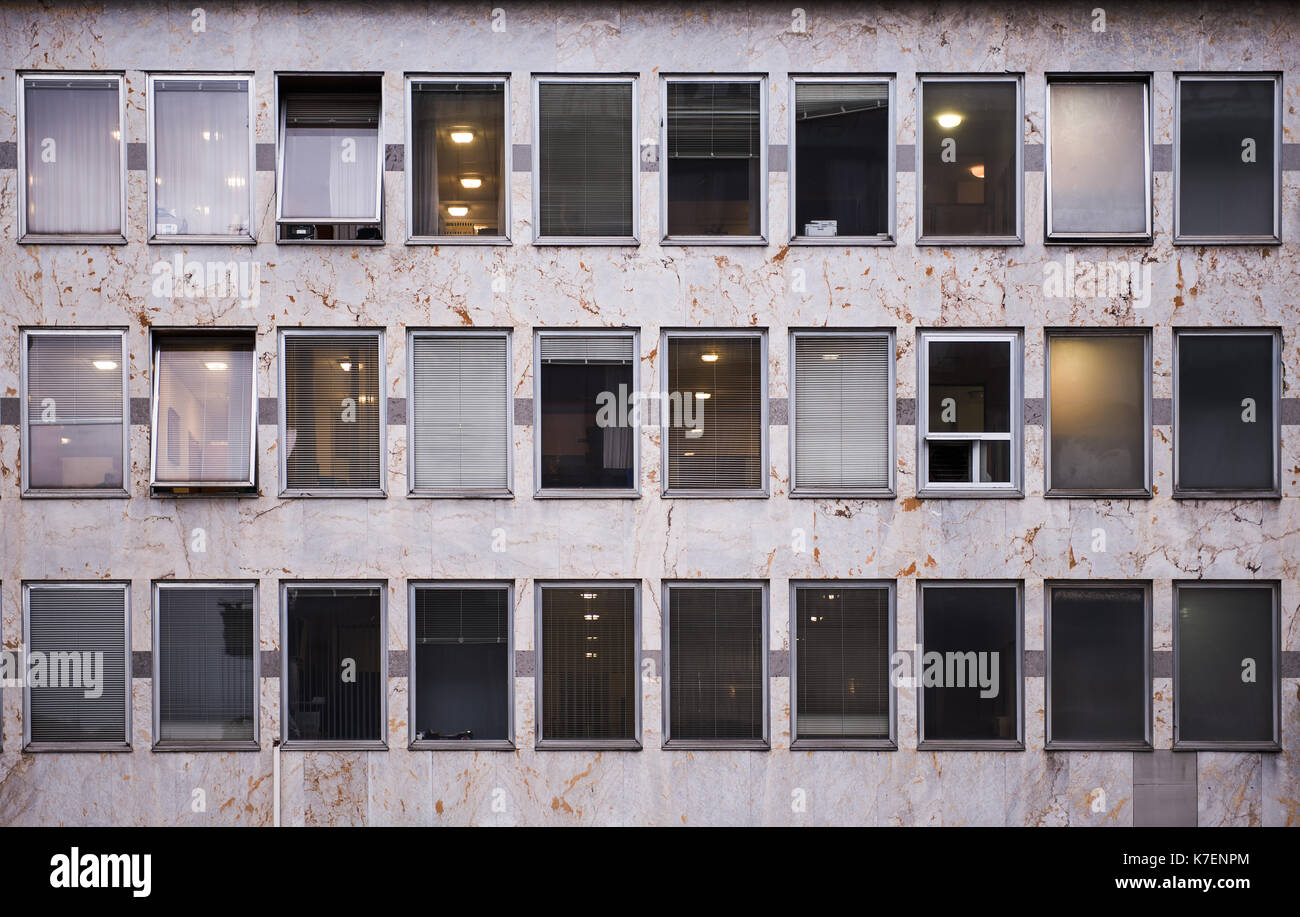 Edificio de oficinas en un centro de distrito, frentes de mármol y persianas venecianas en windows, algunas oficinas iluminado Foto de stock