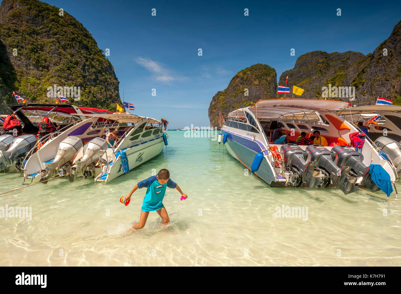 Niño juega entre embarcaciones turísticas alineadas en maya bay, Isla de Ko Phi Phi lee, Tailandia. Foto de stock