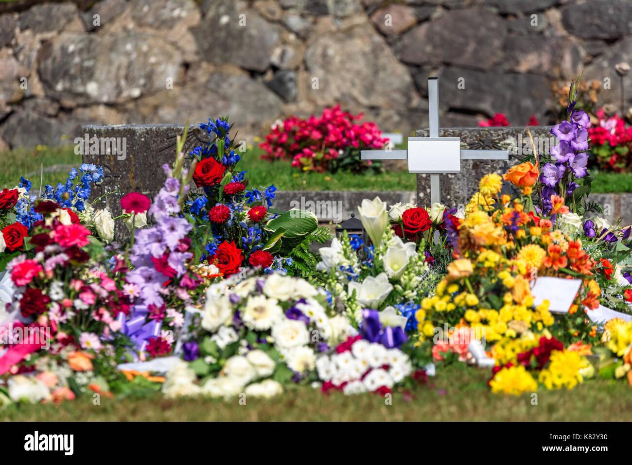 Un montón de flores y la pequeña cruz, después de un entierro en un cementerio. El nombre y el texto eliminado de todas las notas y etiquetas. Foto de stock