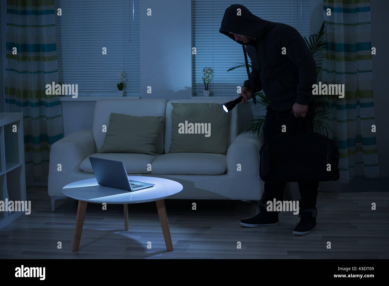 La longitud total del ladrón sosteniendo una linterna a través de ordenador portátil sobre la mesa en casa Foto de stock
