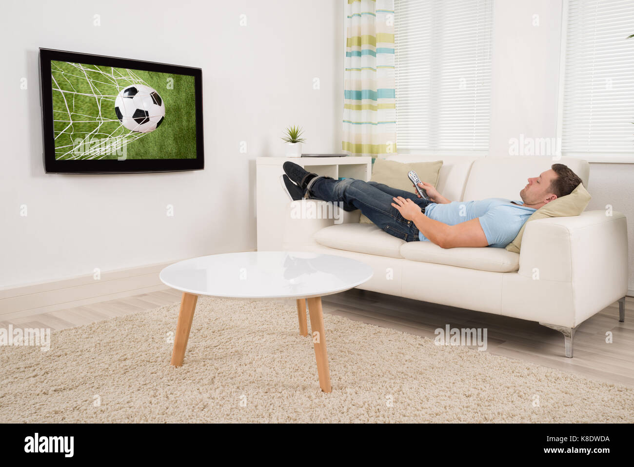 Hombre adulto medio relajado tumbado en el sofá mientras se está viendo partido de fútbol en la televisión en casa Foto de stock