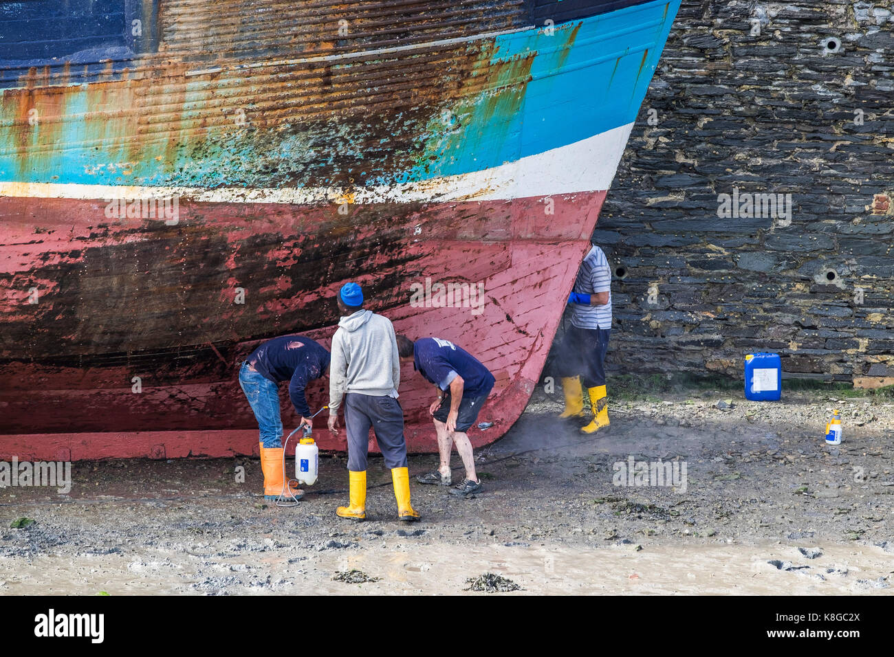 - Los trabajadores de la industria pesquera de inspeccionar el casco de la pesca de arrastre en la marea baja en Padstow Harbour en el norte de la costa de Cornwall. Foto de stock