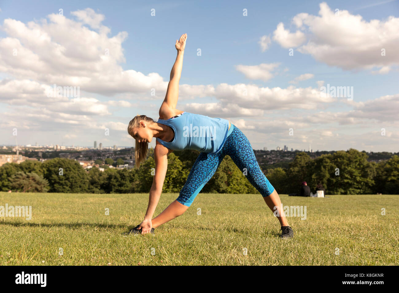Mujer joven practicando yoga en el parque, de pie y agacharse lateralmente Foto de stock