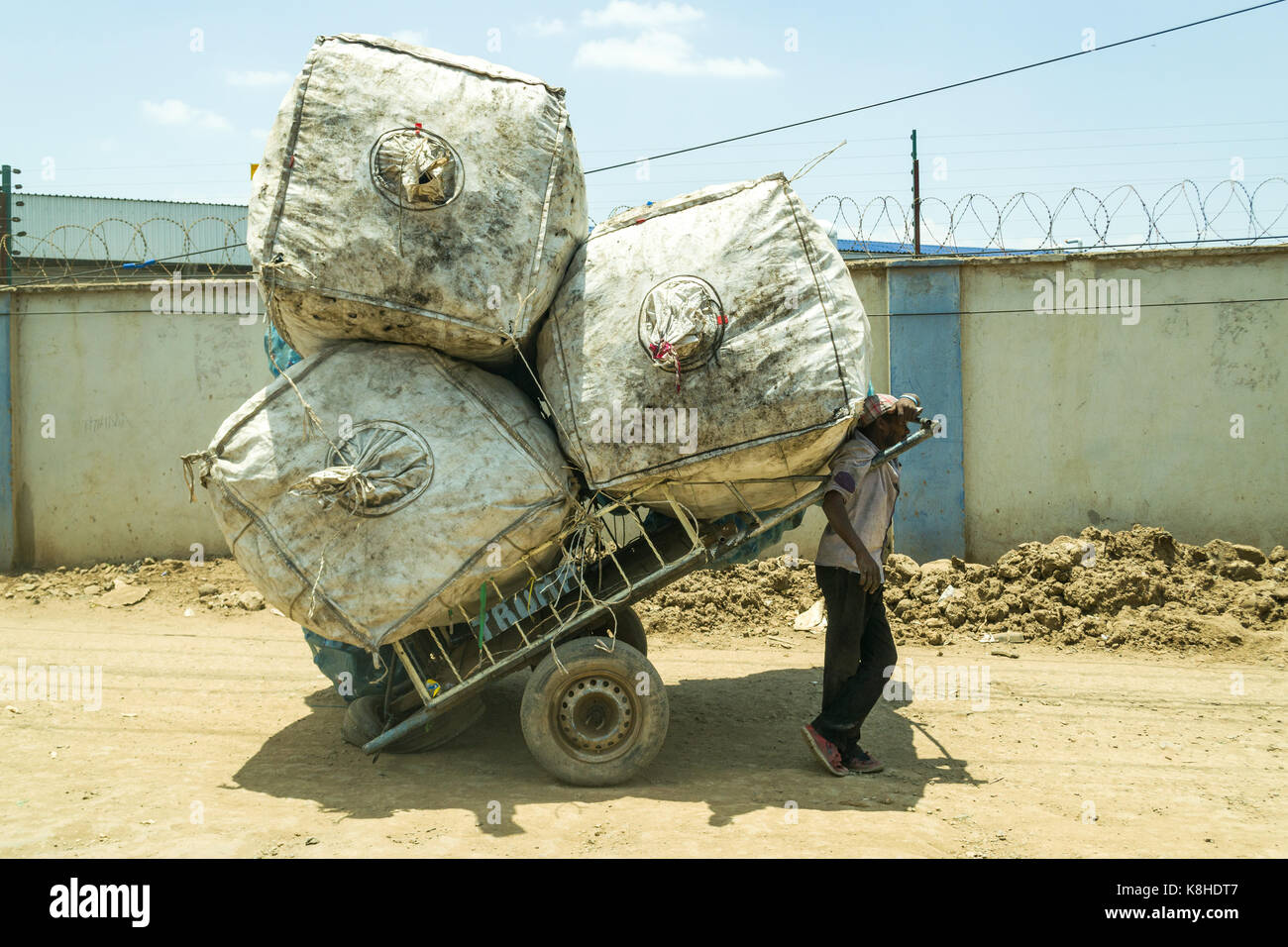 Extractor carrito de mano está descansando en la sombra de enormes sacos llenos de plástico para reciclar, Nairobi, Kenia Foto de stock