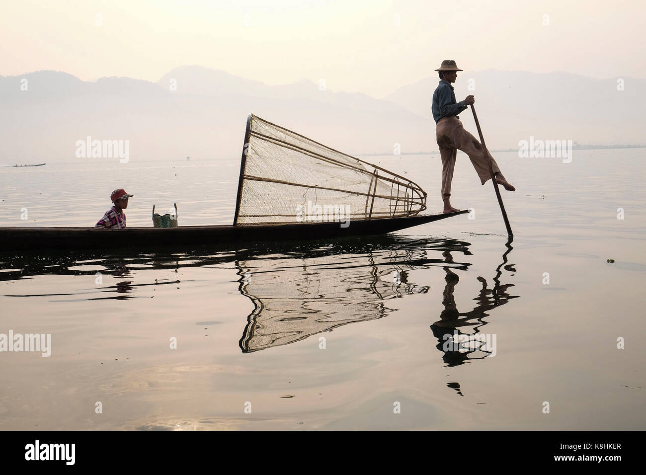 Birmania, Myanmar: pescador en una barcaza en el Lago Inle. Pescador con su hijo en una barcaza y cono de trampa de peces Foto de stock