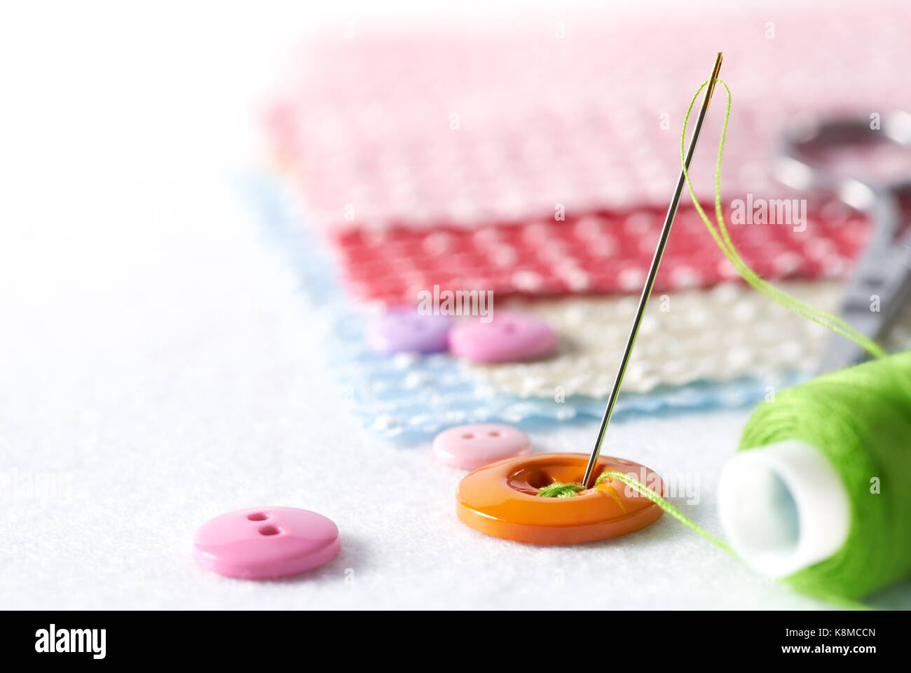 Aguja e hilo de coser con botones sobre fondo blanco. Foto de stock