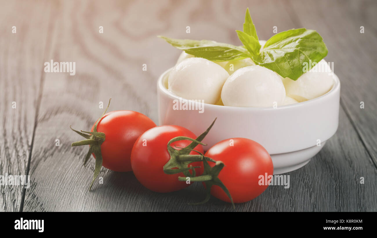 Pequeñas bolas de mozzarella en blanco tazón con tomates ciruela Foto de stock