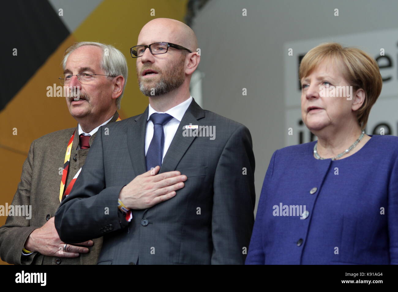 Giessen, Alemania. 21 de septiembre de 2017. Angela Merkel, Canciller de Alemania, celebra un discurso de campaña electoral como líder de la Unión Demócrata Cristiana y como líder candidato como canciller federal para las elecciones federales del Bundestag (24 de septiembre de 2017) en Brandplatz en Giessen, Alemania. Aquí: Angela Merkel (derecha) canta el himno nacional alemán con Hans-Jürgen Irmer (izquierda), la conconstancia candidata directa de la CDU 172/Lahn-Dill 2, y Peter Tauber (centro), secretario general de la CDU. Crédito: Christian Lademann Foto de stock