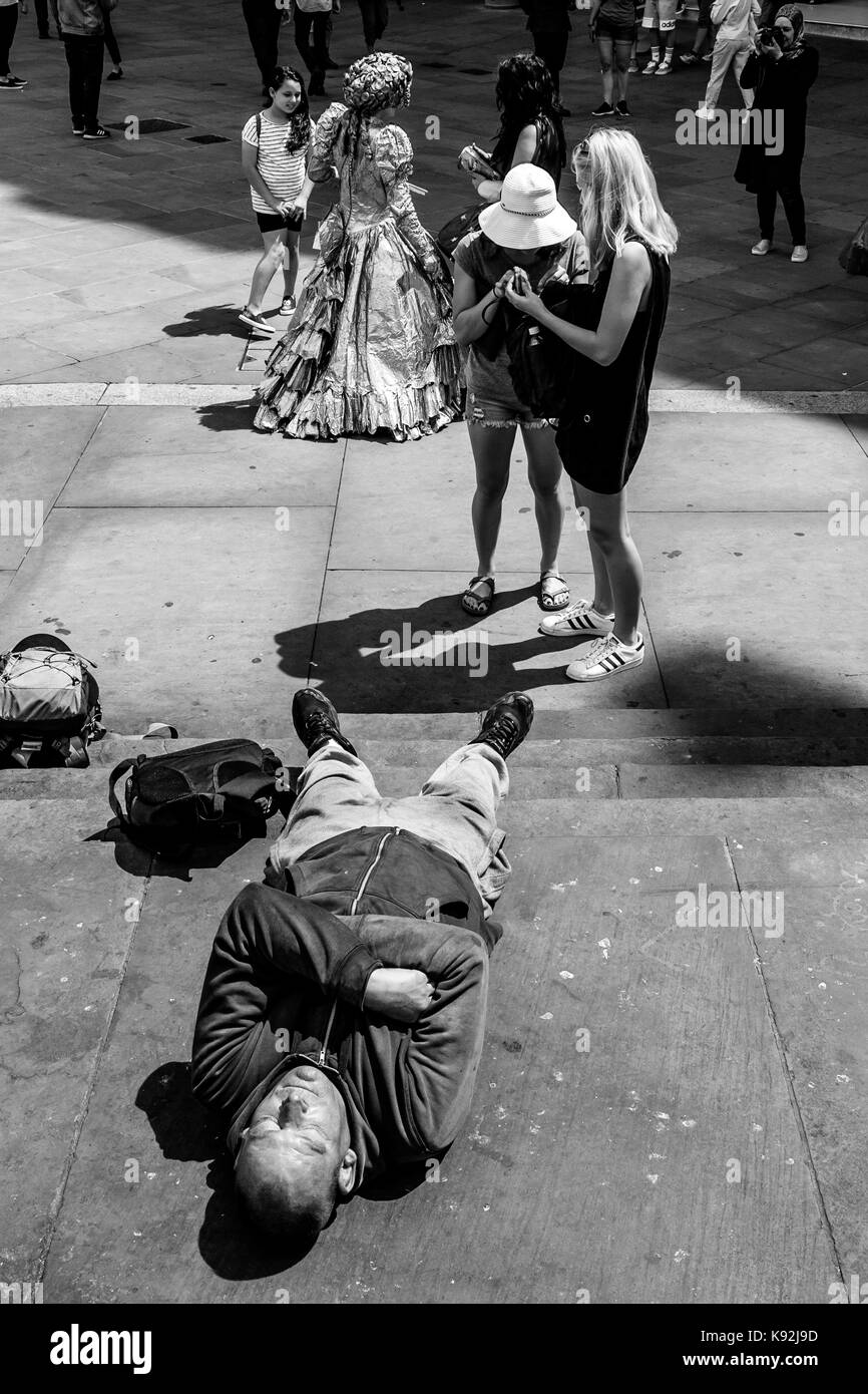 Un hombre dormido sobre los pasos de la Estatua de Eros, Piccadilly Circus, Londres, Reino Unido. Foto de stock