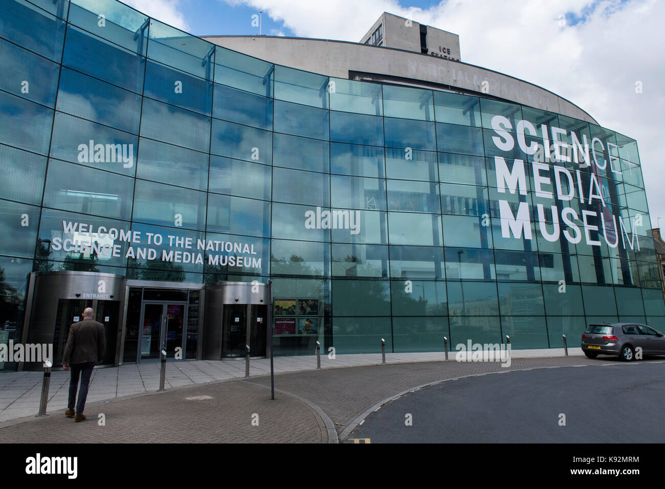 Vista exterior del Museo de la ciencia y medios (Bradford, West Yorkshire, Inglaterra, Reino Unido), curvos, con una impresionante fachada acristalada - el hombre camina a la entrada. Foto de stock