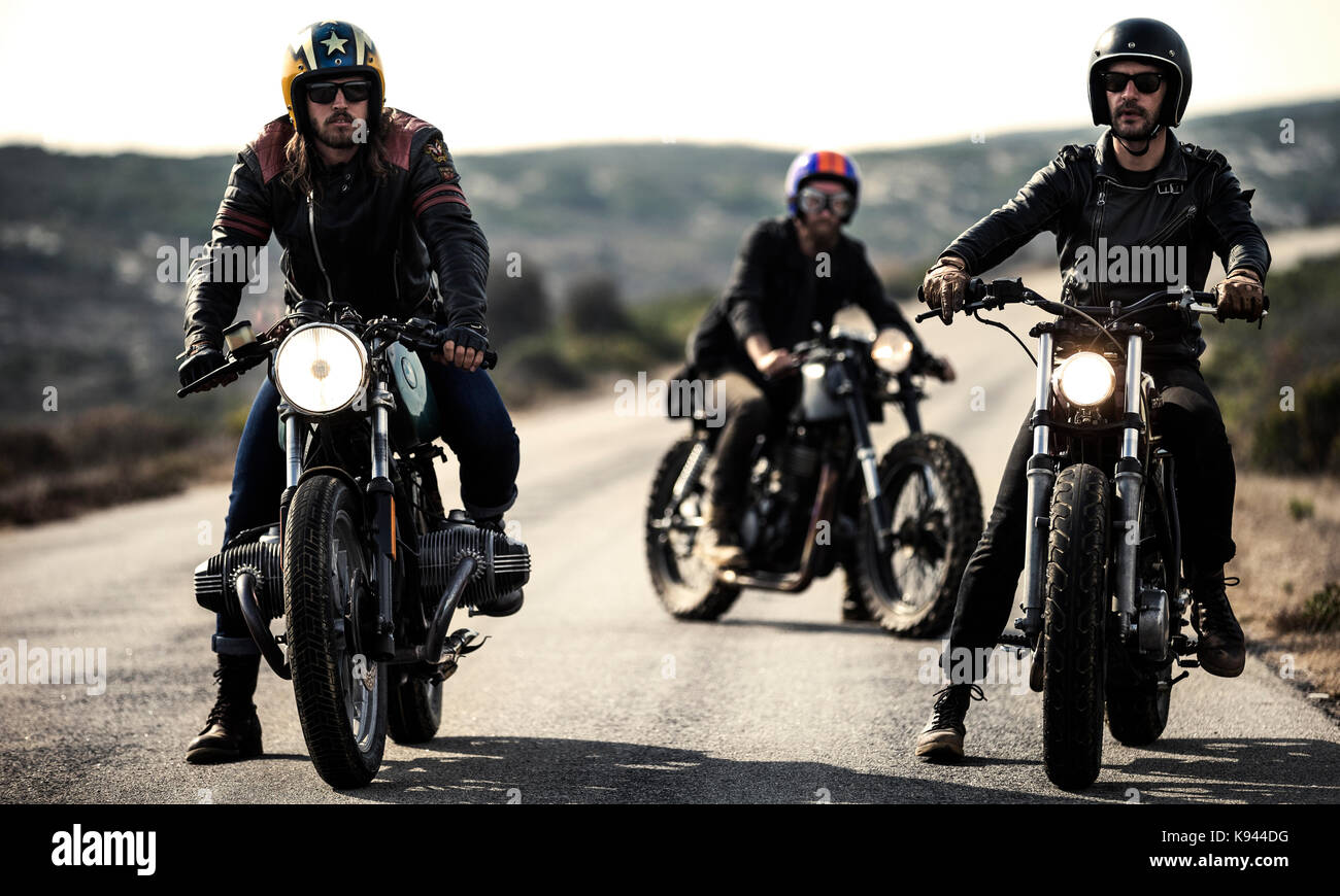 Tres hombres vestidos de cara abierta cascos y gafas sentado en cafe racer  motos en caminos rurales Fotografía de stock - Alamy