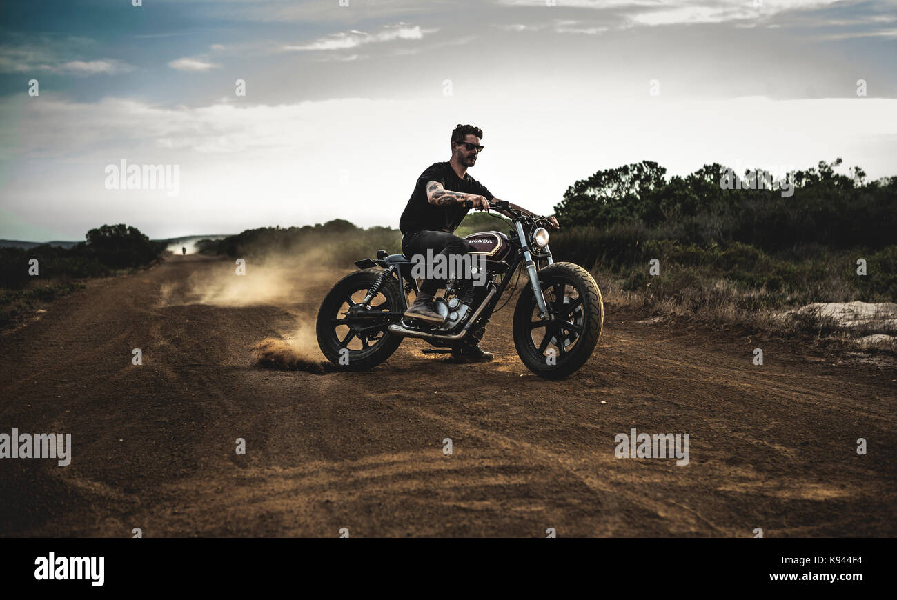 Hombre con gafas de sol Caballo Cafe Racer moto por un polvoriento