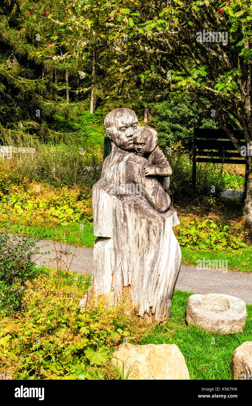 Un tronco de madera tallada en una escultura de una mujer que sostiene a un bebé, iluminado por la luz del sol de otoño en la zona boscosa de Queen's View visitor center Foto de stock