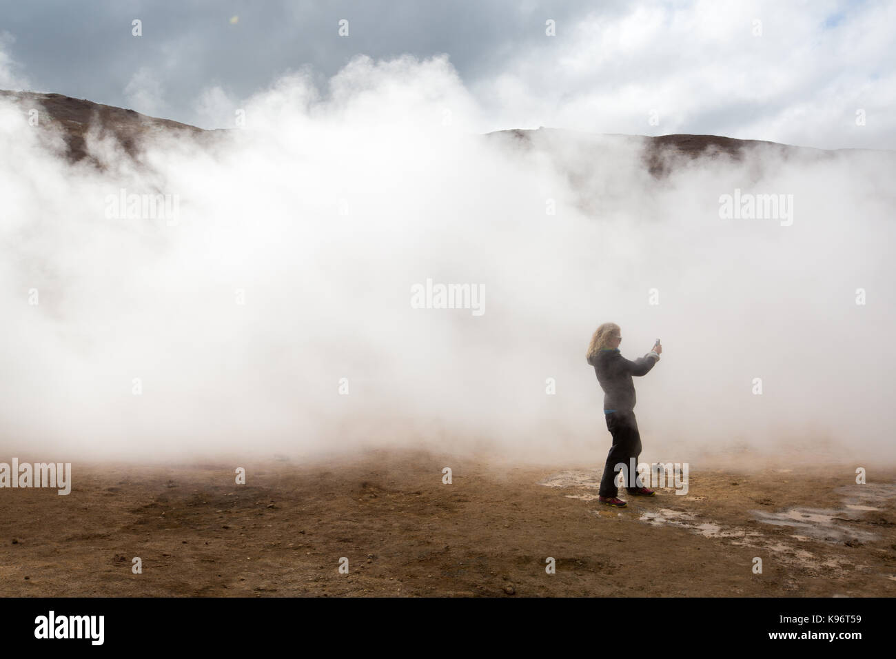 Una mujer fotografías entre las humeantes ollas de barro área geotérmica cerca del lago Myvatn. Foto de stock