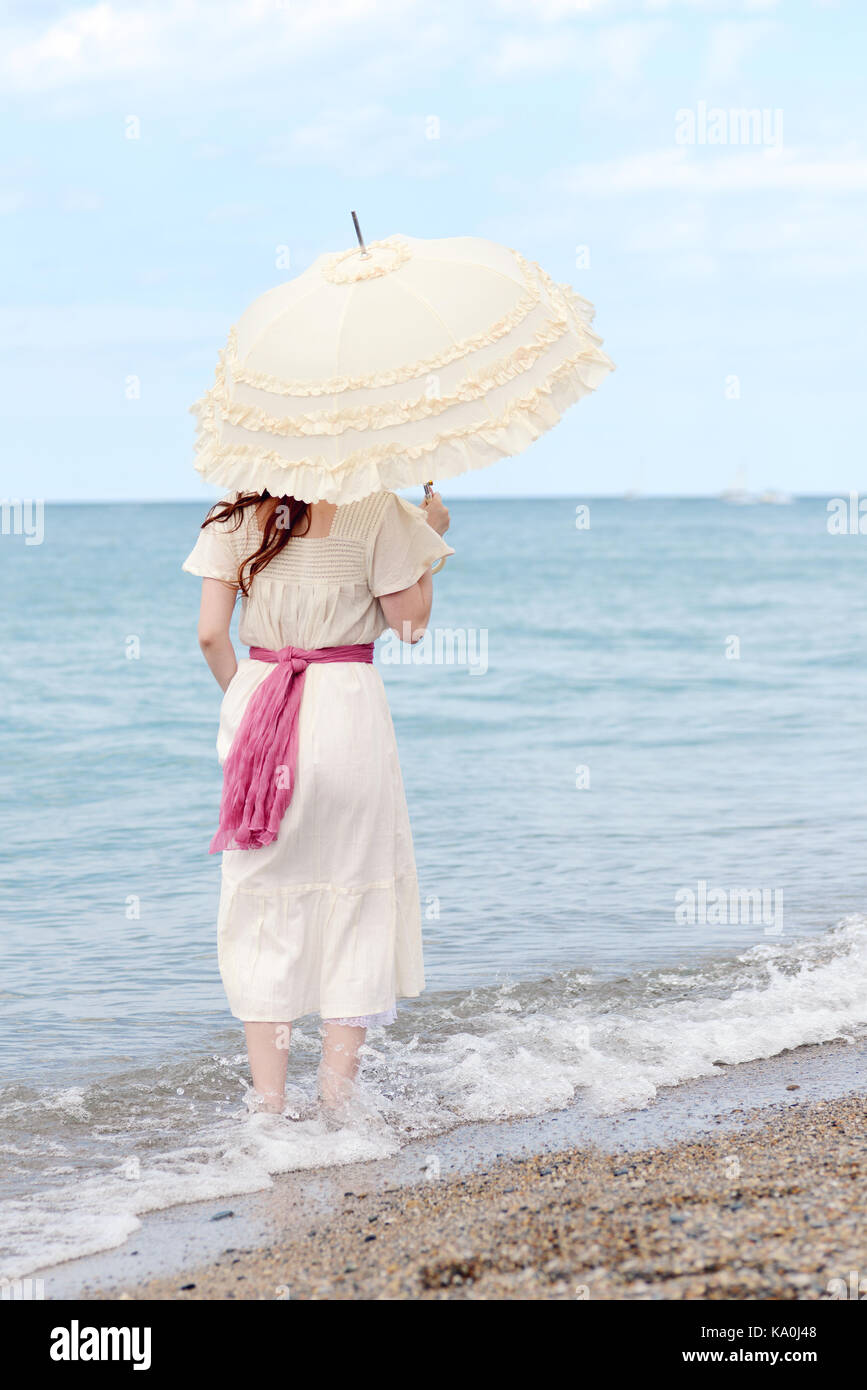 Vintage mujer con sombrilla de pie en el agua en la playa Fotografía de  stock - Alamy