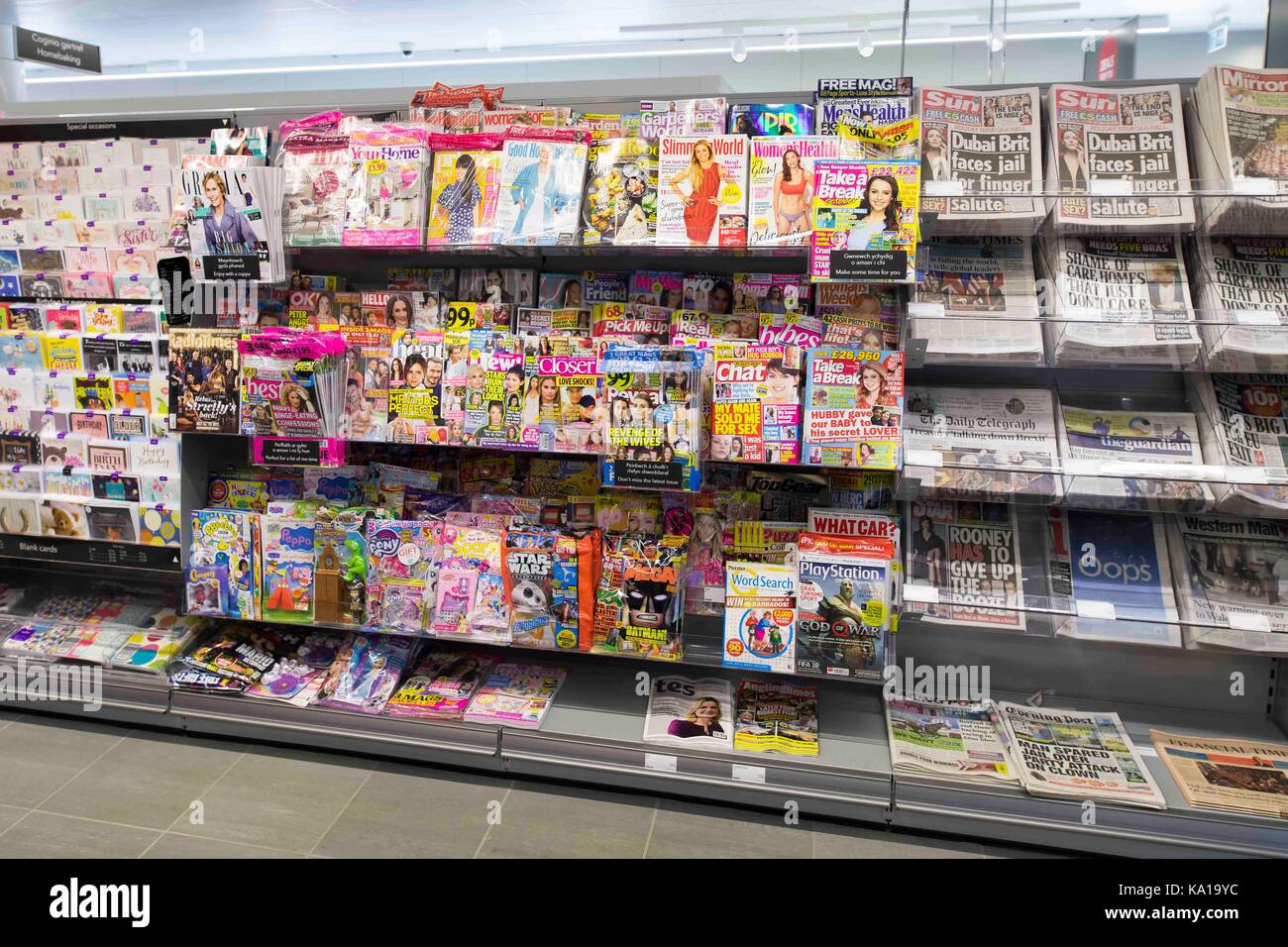 Periódicos y revistas en la pantalla en un estante en un supermercado quiosco tienda. Foto de stock