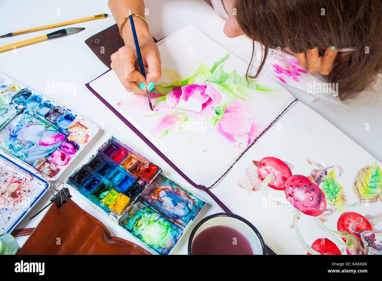 Un close-up artist pinta y dibuja en el álbum para dibujar un cepillo de  madera fina de color rosa con colores de acuarela, sobre la mesa es una  funda de cuero con