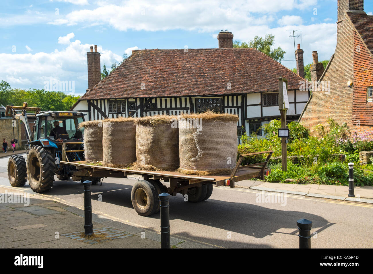 Fardos de paja en un tractor va a la comunidad a través de la pintoresca ciudad de Battle, East Sussex, Inglaterra, Reino Unido. Foto de stock